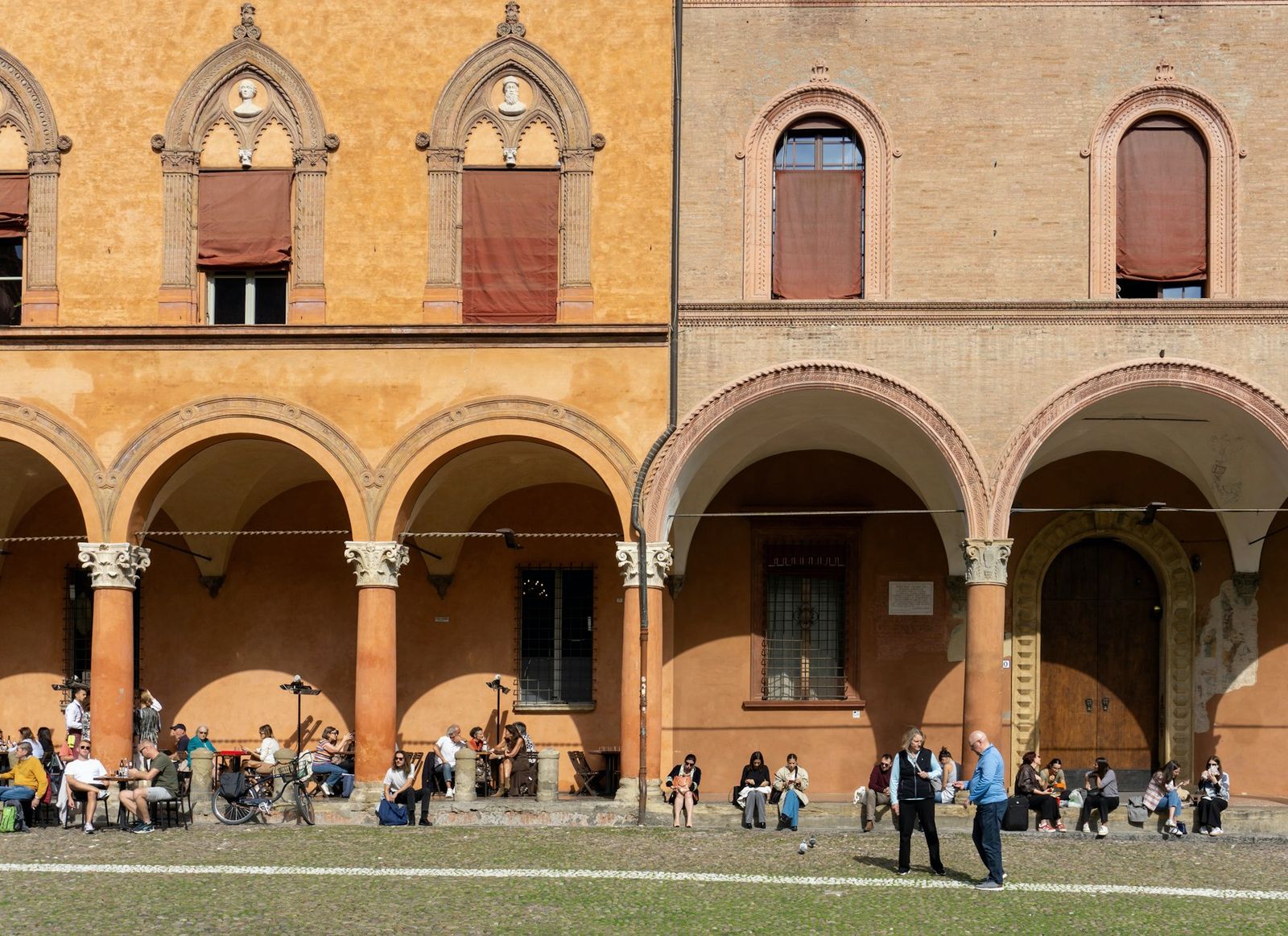 Bologna arcade with orange porticoes and people walking and sitting on the square