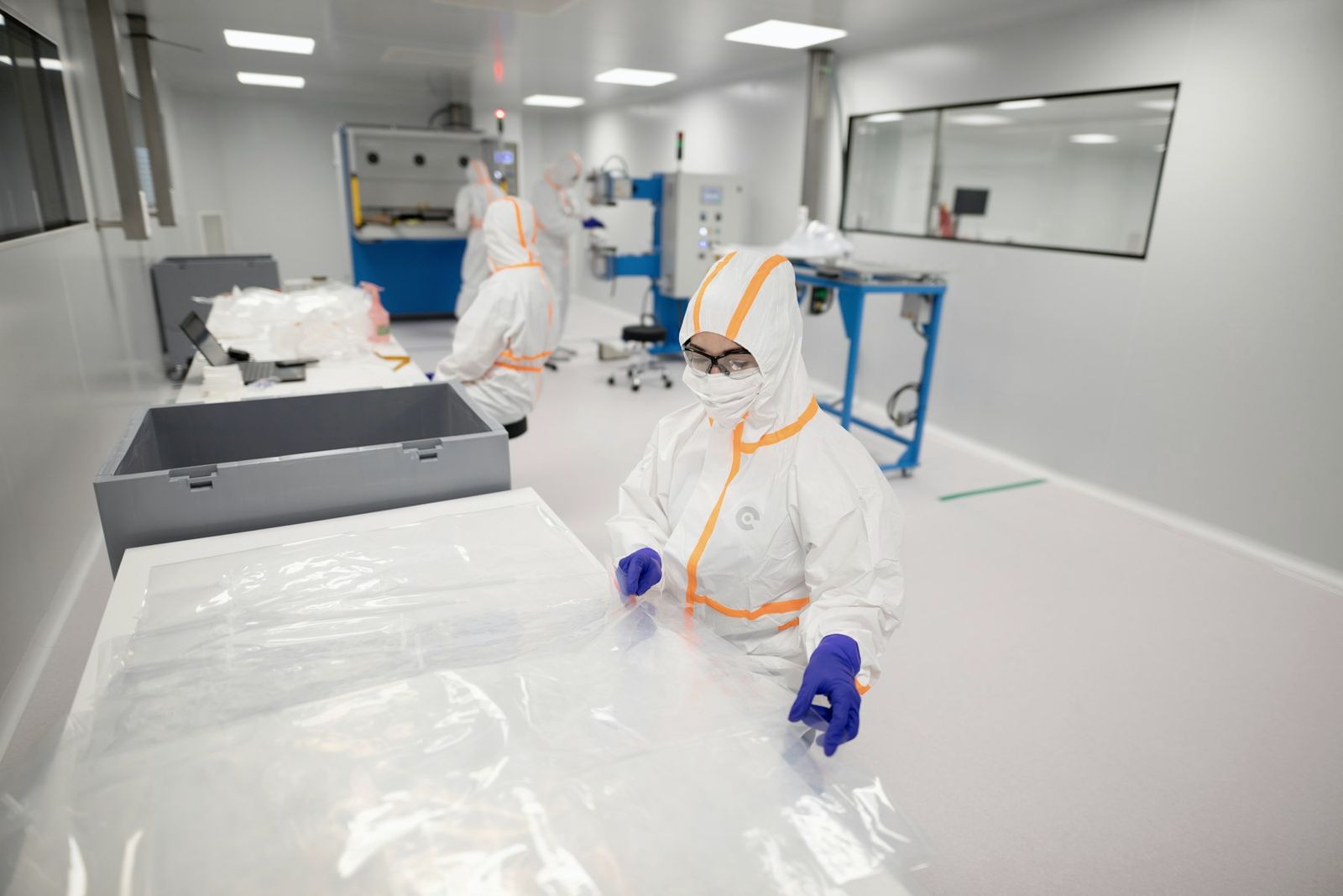 Operator in full cleanroom gown, mask and gloves handling sterile plastic film