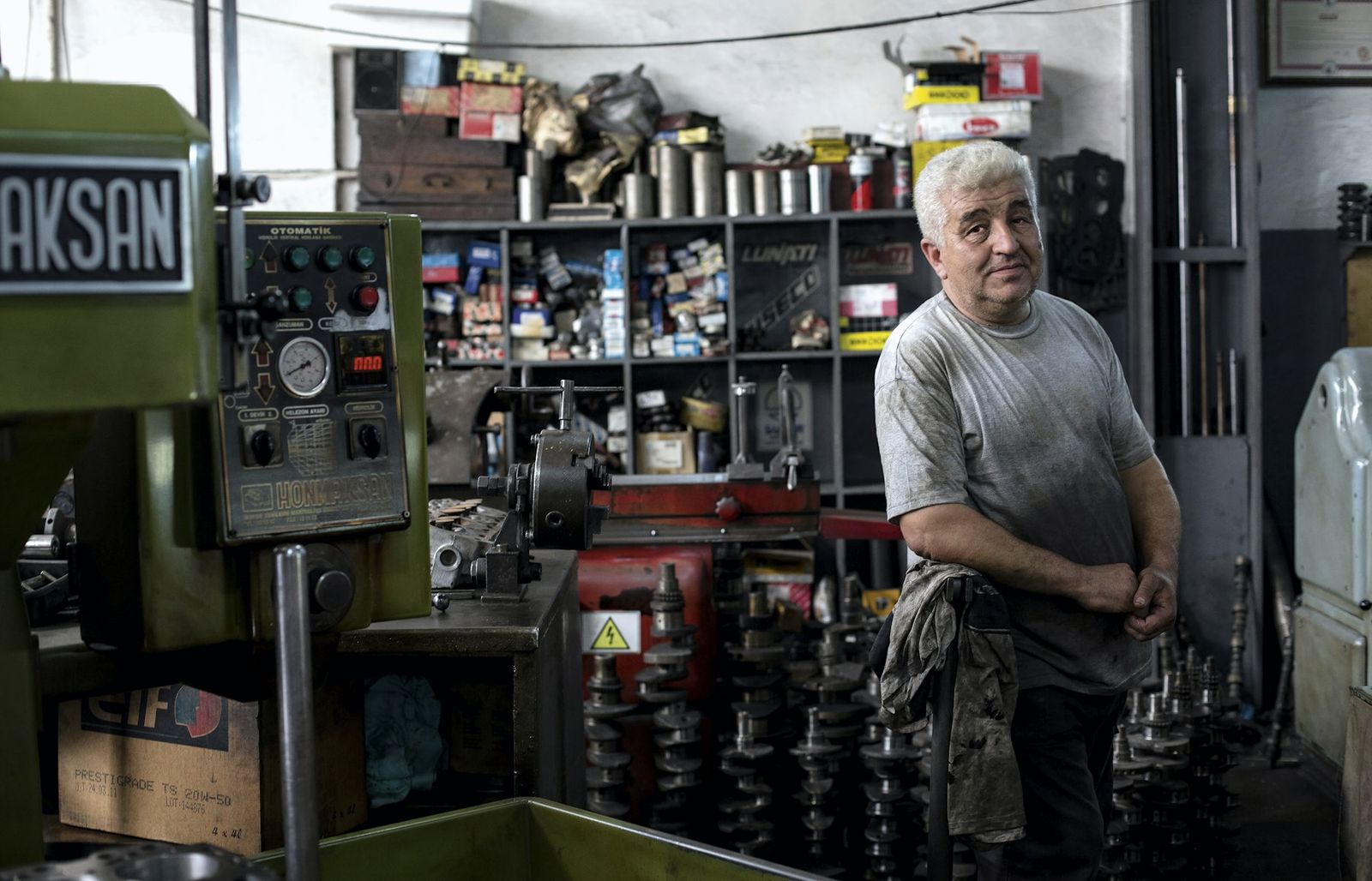 Older male machinist standing beside workshop machinery, looking at the camera