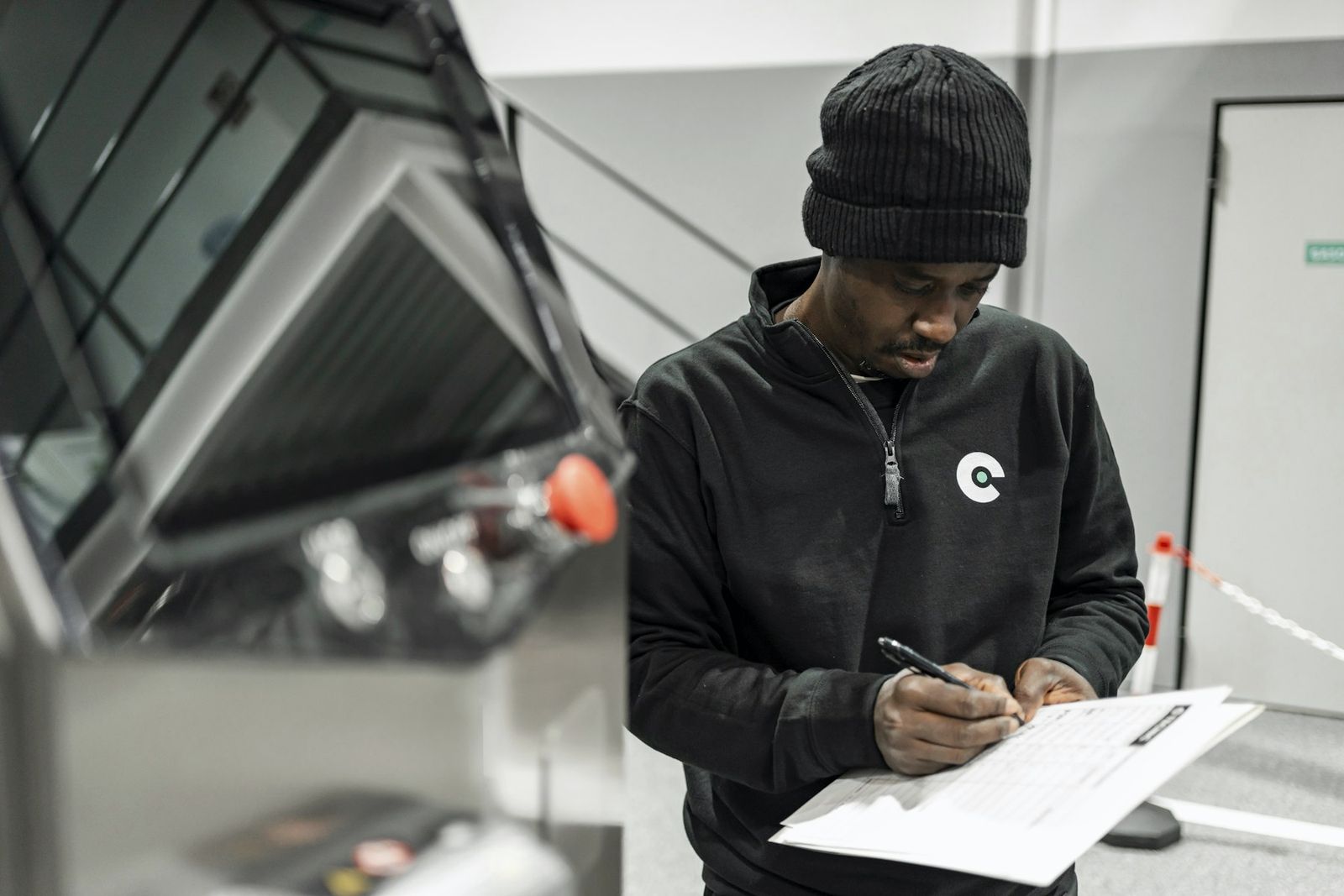 Technician in a dark jacket filling in a paper checklist beside industrial equipment