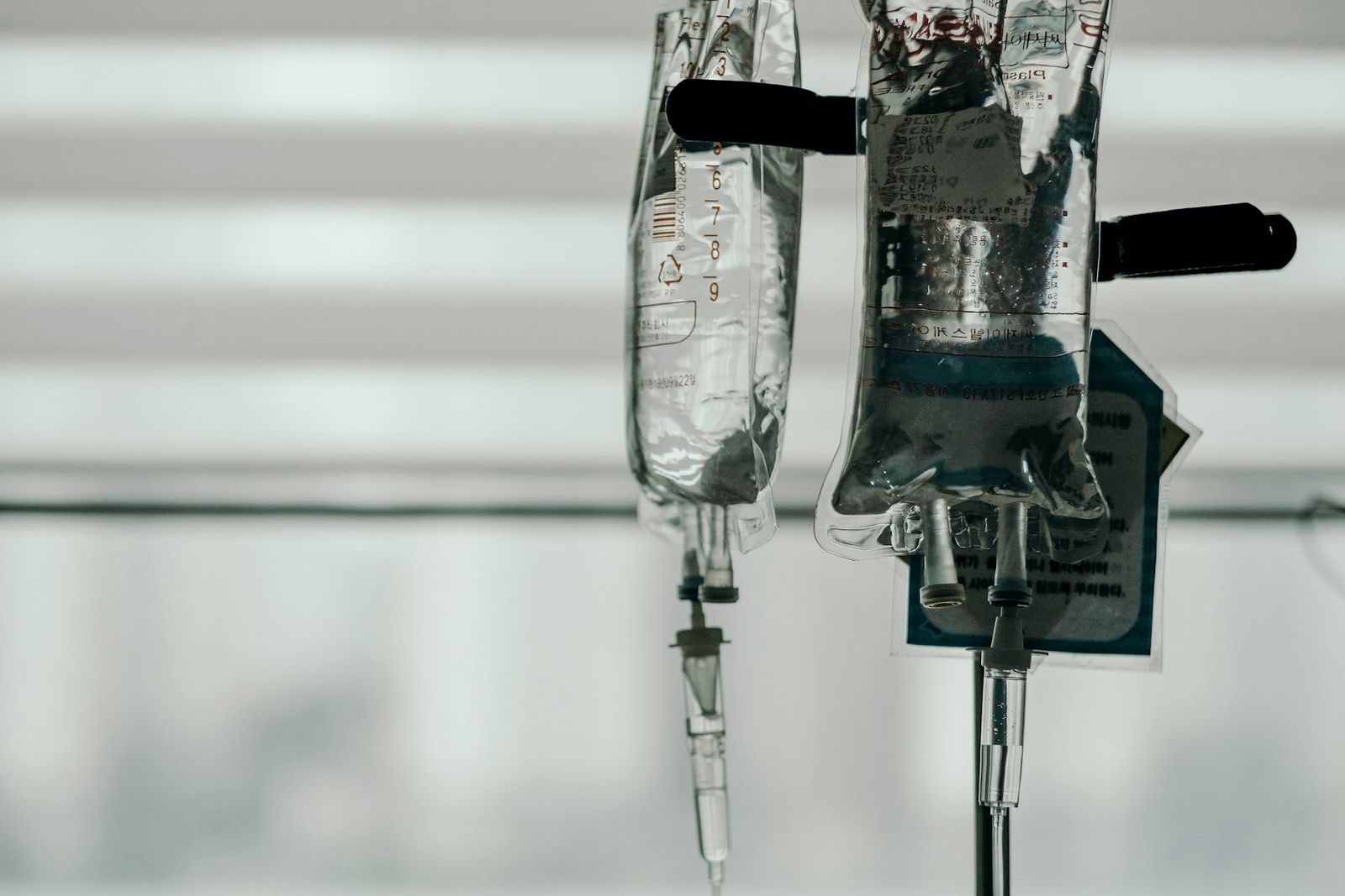 Two IV infusion bags hanging from a stand against soft daylight